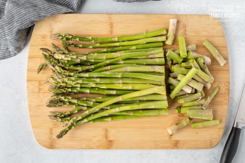 Cutting off the ends of asparagus with a knife on a cutting board.