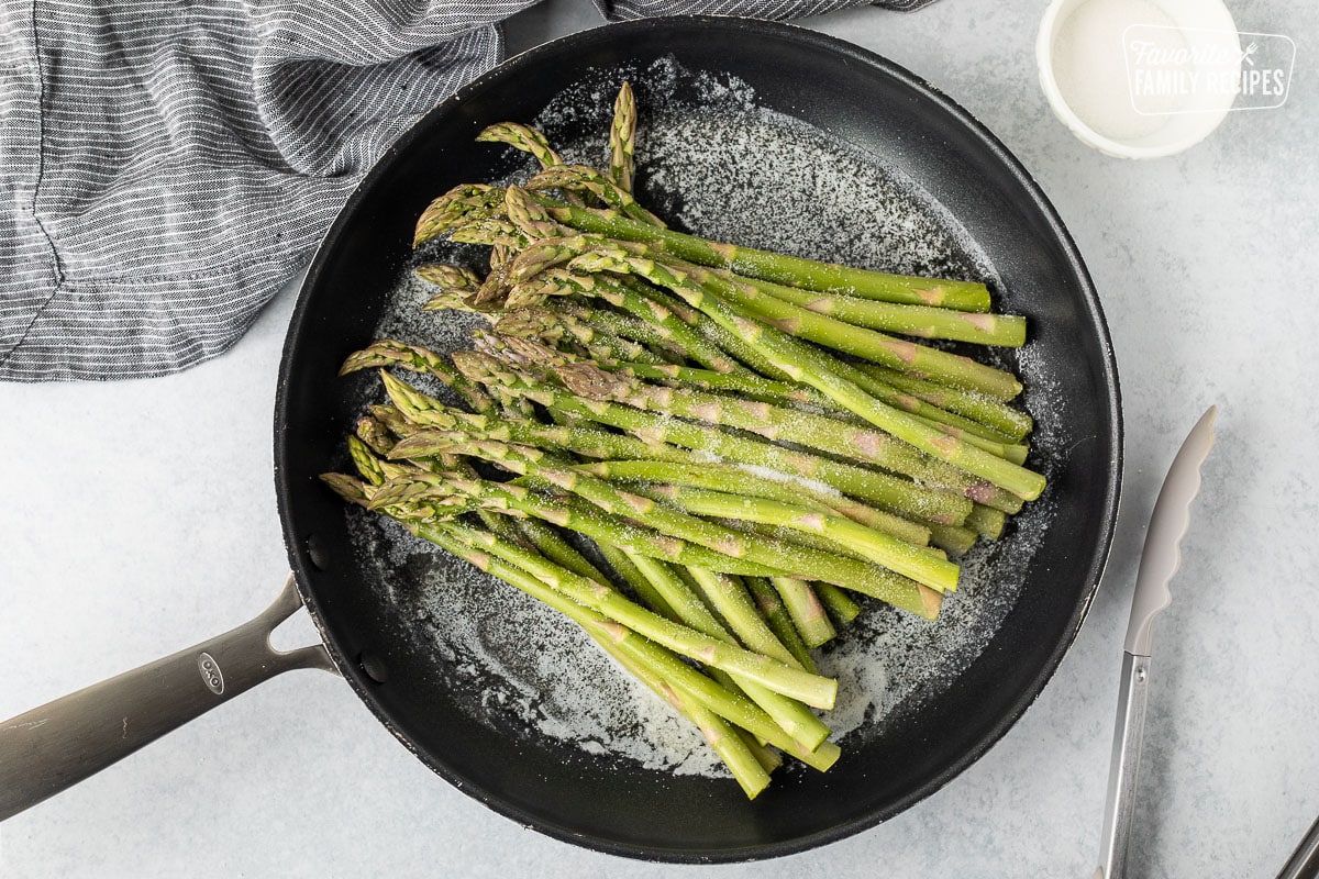 Skillet with melted butter, raw asparagus and sugar. Tongs on the side.