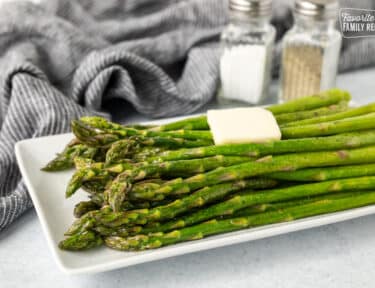 Side view of Sweet Sautéed Asparagus with butter and salt and pepper in the background.