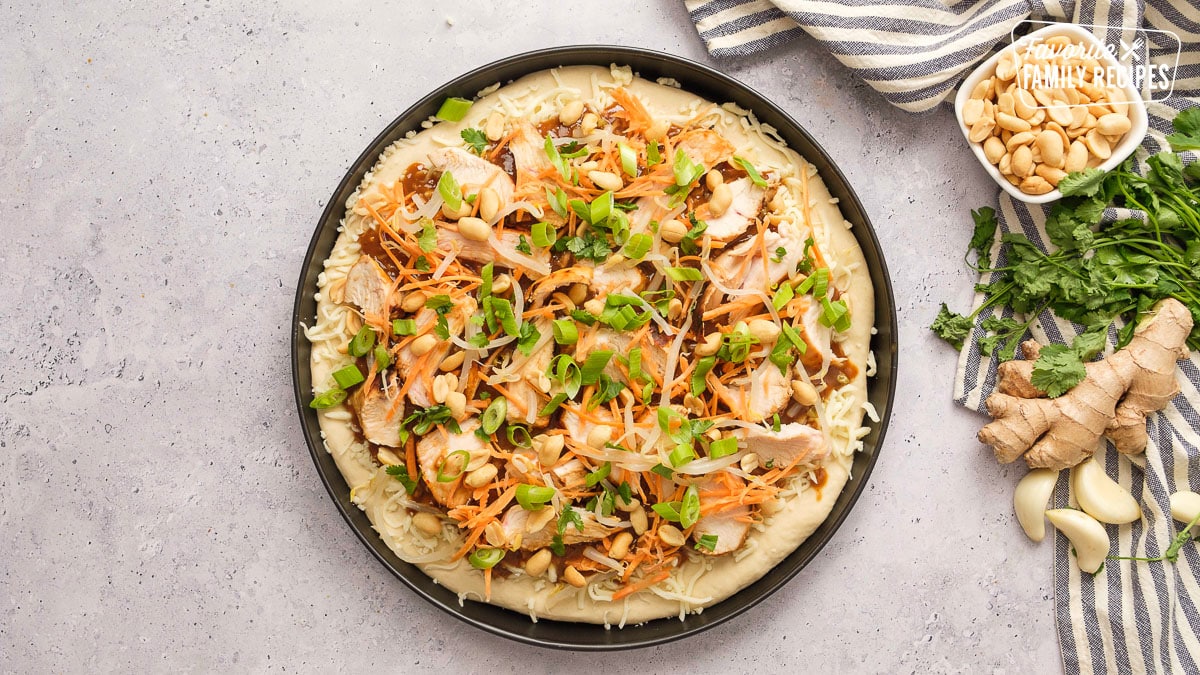 Unbaked Thai chicken pizza in a black pizza pan.