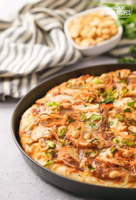 A black pizza pan with Thai chicken pizza baked in it.