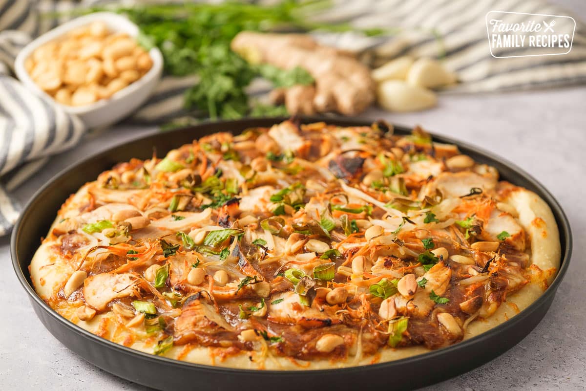 Thai chicken pizza in a black pizza pan. 