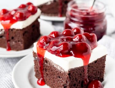 Three slices of Chocolate Cherry Cake on plates next to jar of Cherry filling.