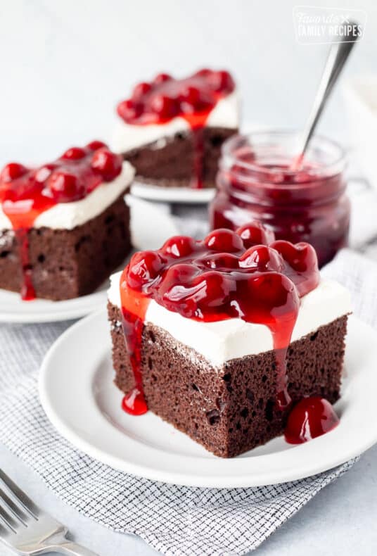Three slices of Chocolate Cherry Cake on plates next to jar of Cherry filling.