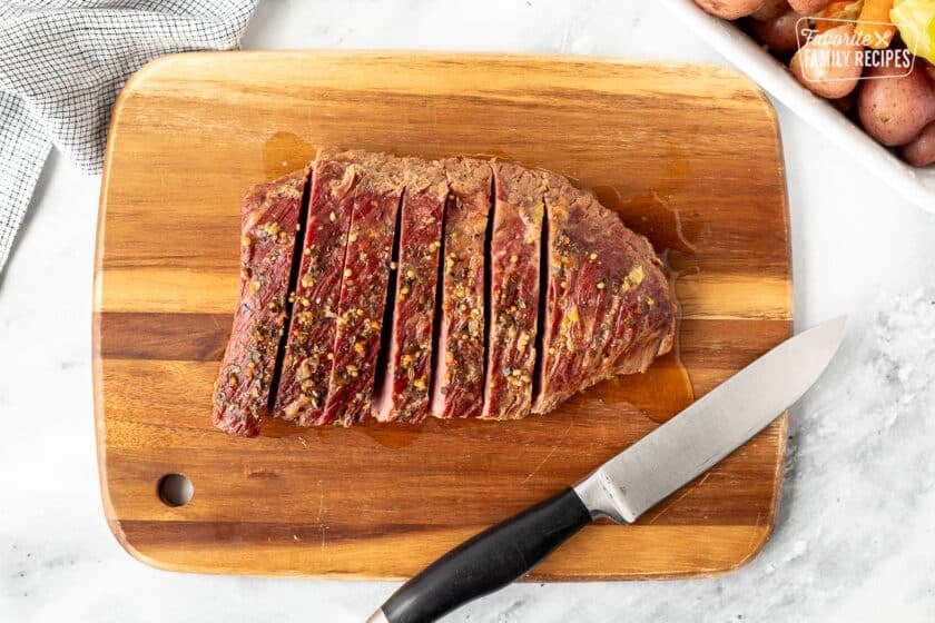 Cut Corned Beef brisket on a cutting board with a knife next to cooked vegetables on the side. and Cabbage