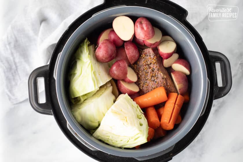 Raw cabbage, red potatoes and carrots in an instant pot over cooked corned beef.