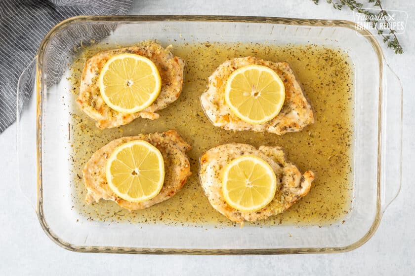 Baking dish with four chicken breasts and fresh sliced lemons on top.