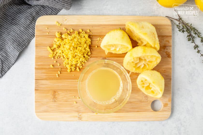 Cutting board with zested lemons and glass cup with fresh lemon juice. Squeezed lemons on the side.