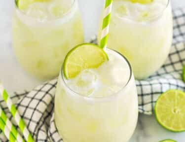 Three glasses of Brazilian Limeade topped with lime wedges and green striped straws