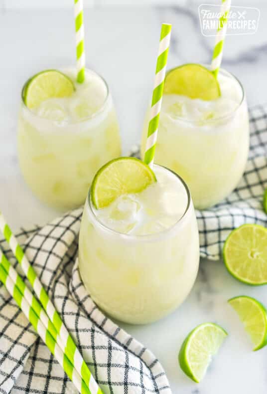 Three glasses of Brazilian Limeade topped with lime wedges and green striped straws