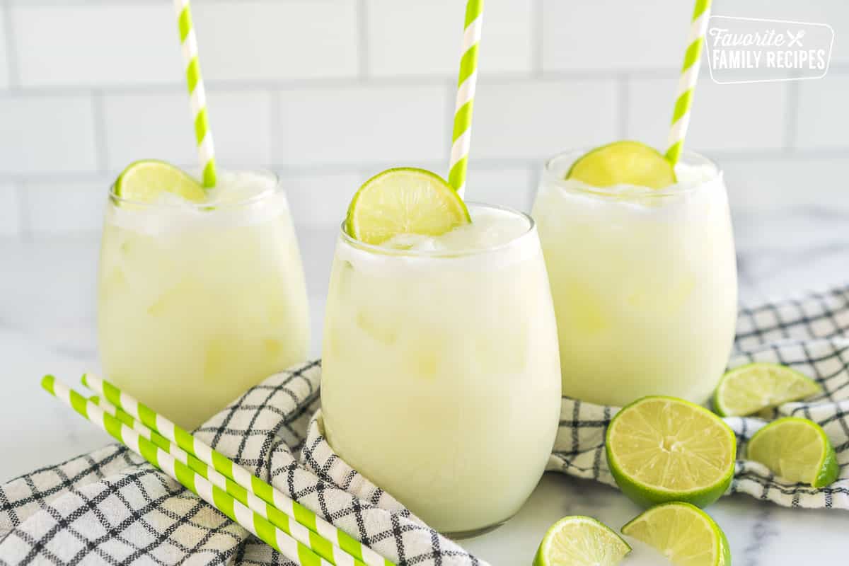 Three glasses of Brazilian Limeade topped with lime wedges and green striped straws