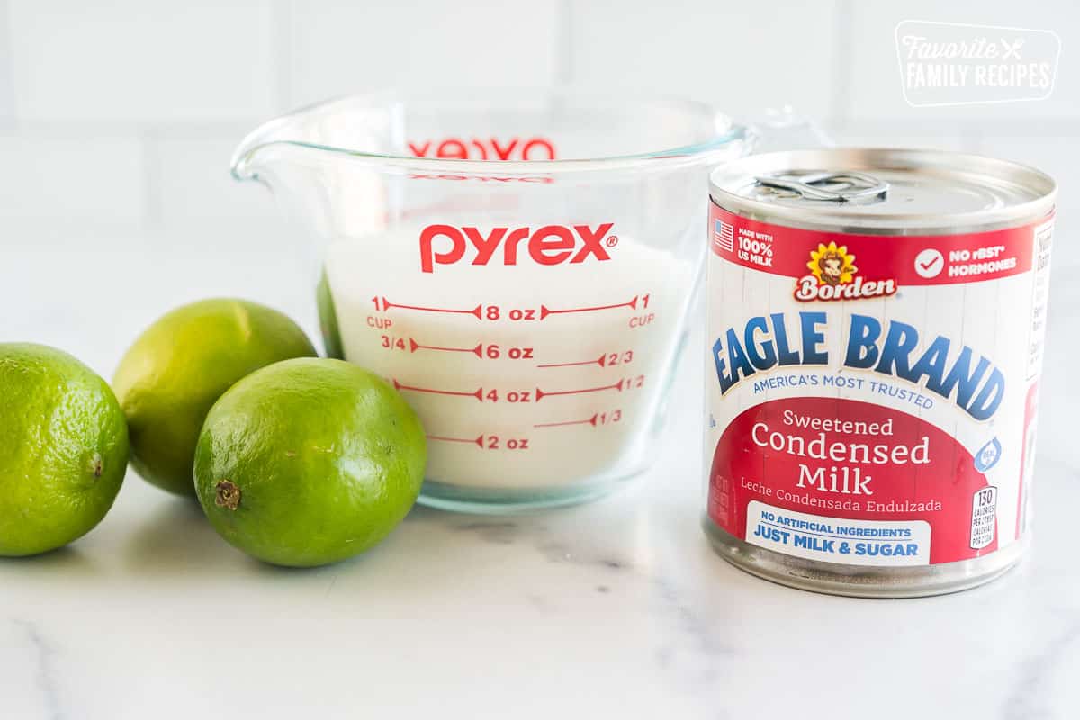 Limes, a measuring cup of sugar, and a can of sweetened condensed milk on the counter