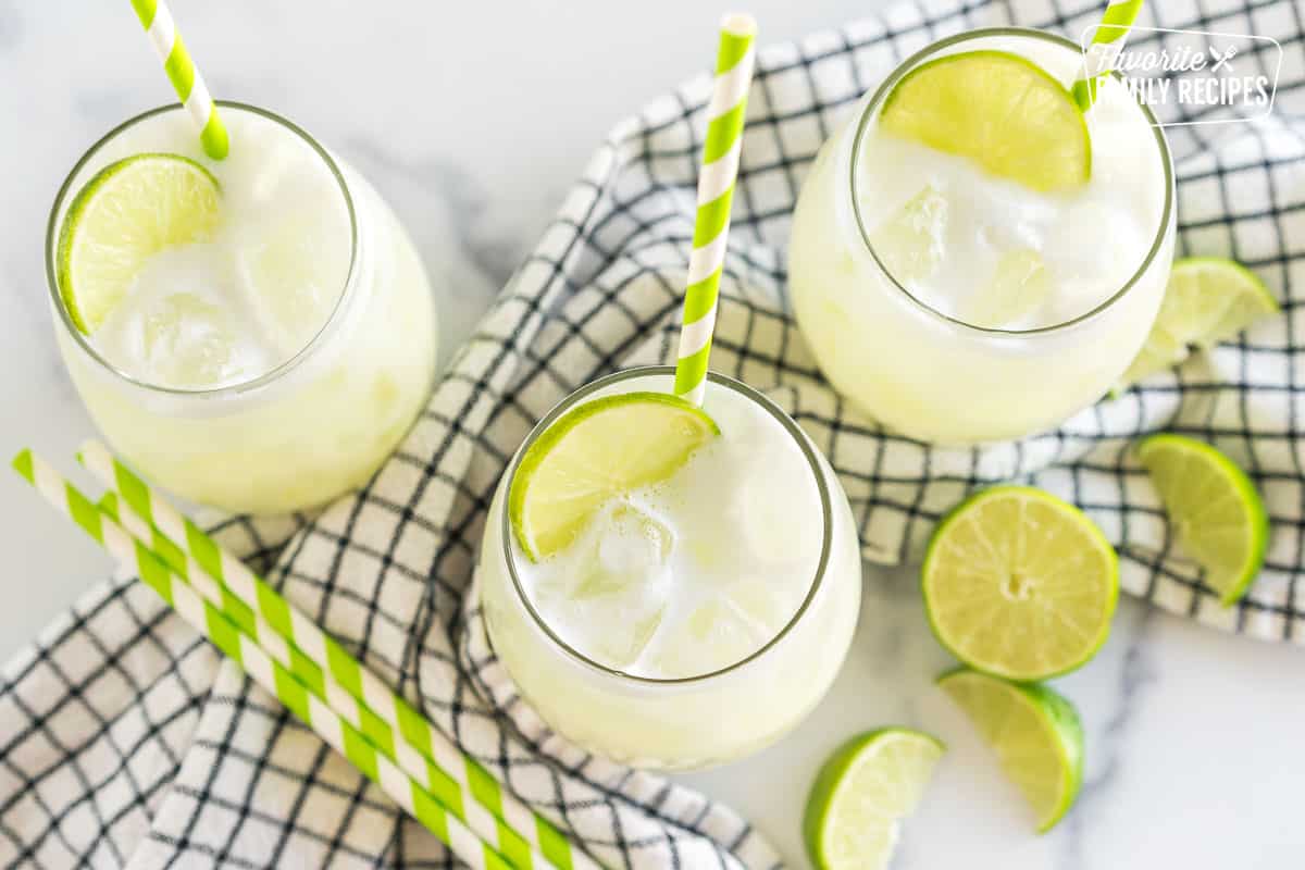 Three glasses of Brazilian Limeade topped with lime wedges and green striped straws