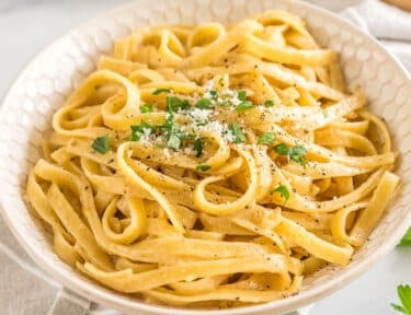 Buttered Noodles in a bowl topped with parsley, pepper, and parmesan