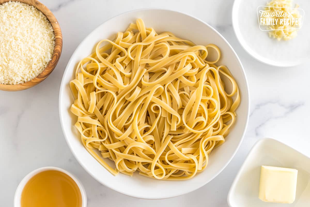 A bowl of pasta surrounded by small bowls of parmesan, chicken stock, garlic, and butter