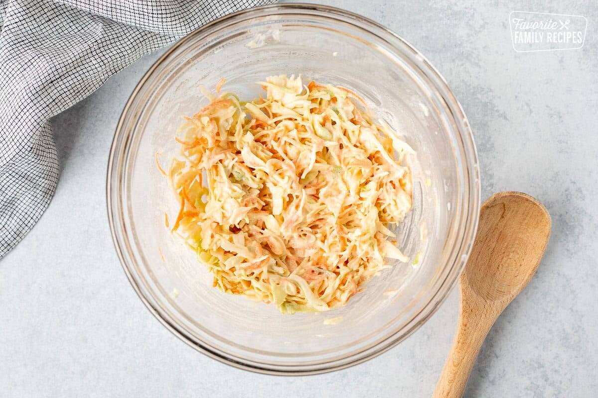 Bowl of mixed coleslaw. Wooden spoon on the side.