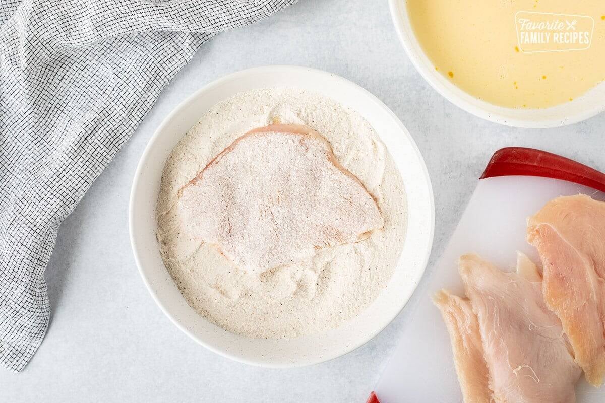 Chicken breast in bowl of flour mixture.