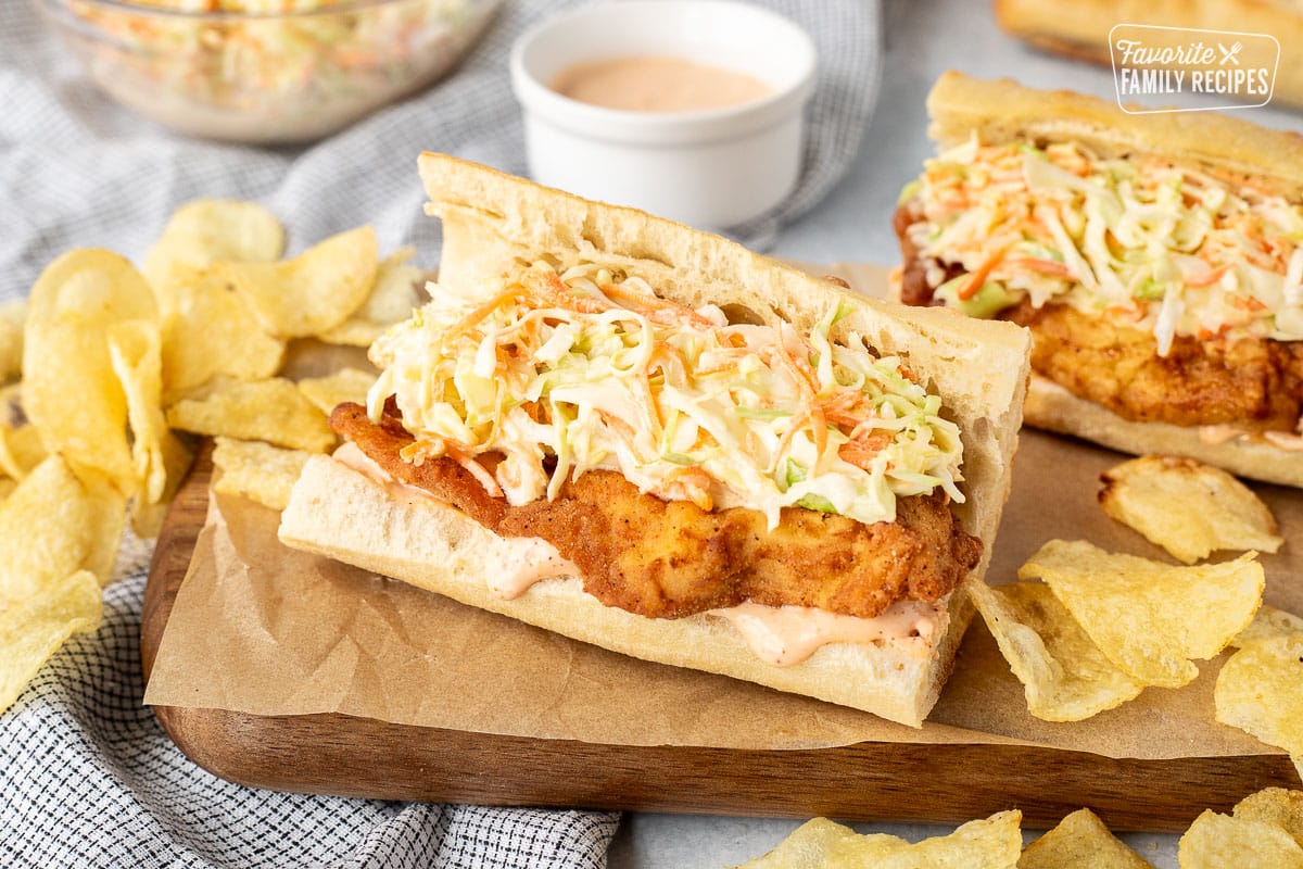 Two Cajun Fried Chicken Po'Boys on a cutting board with chips.