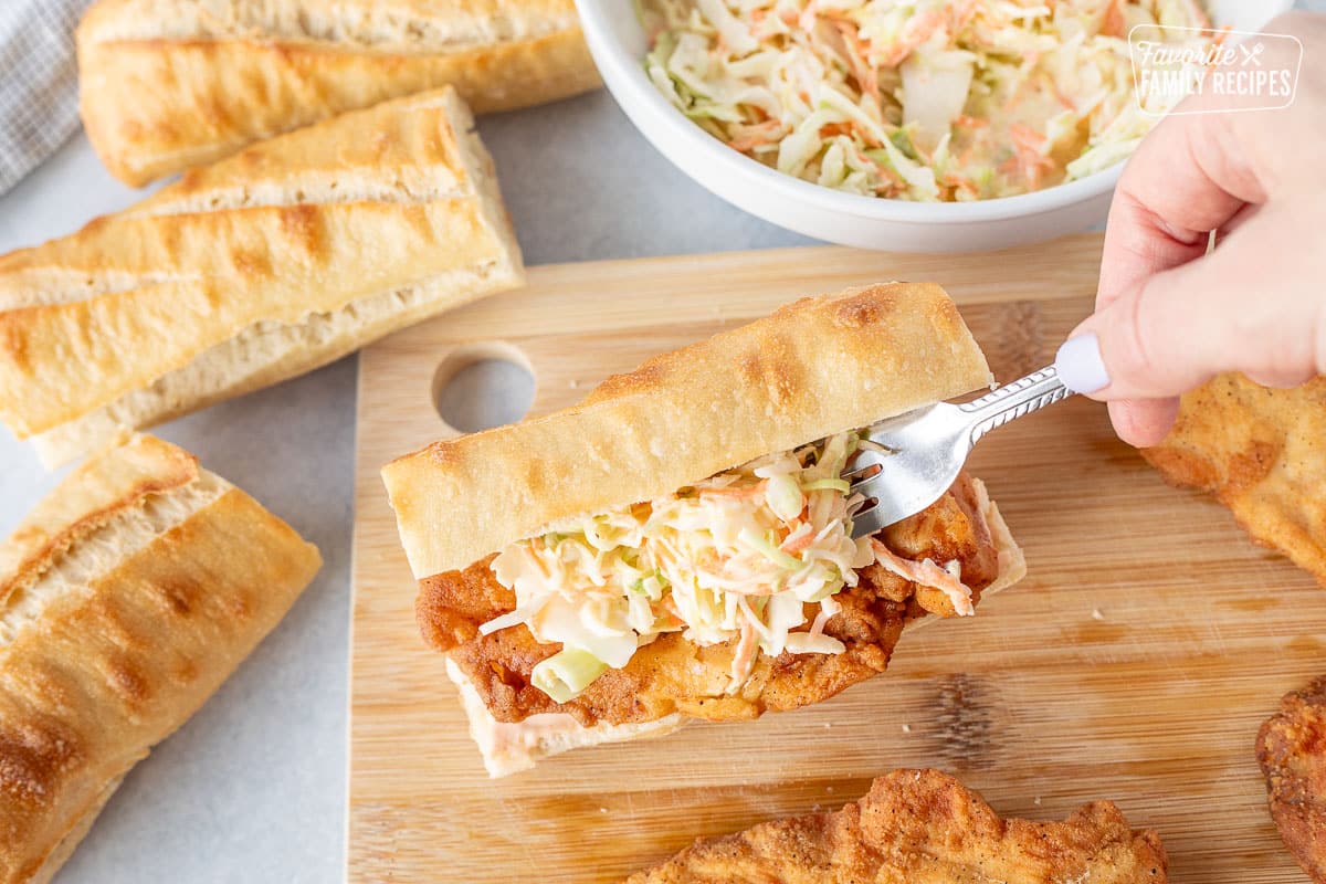 Placing coleslaw on top of chicken breast in roll.
