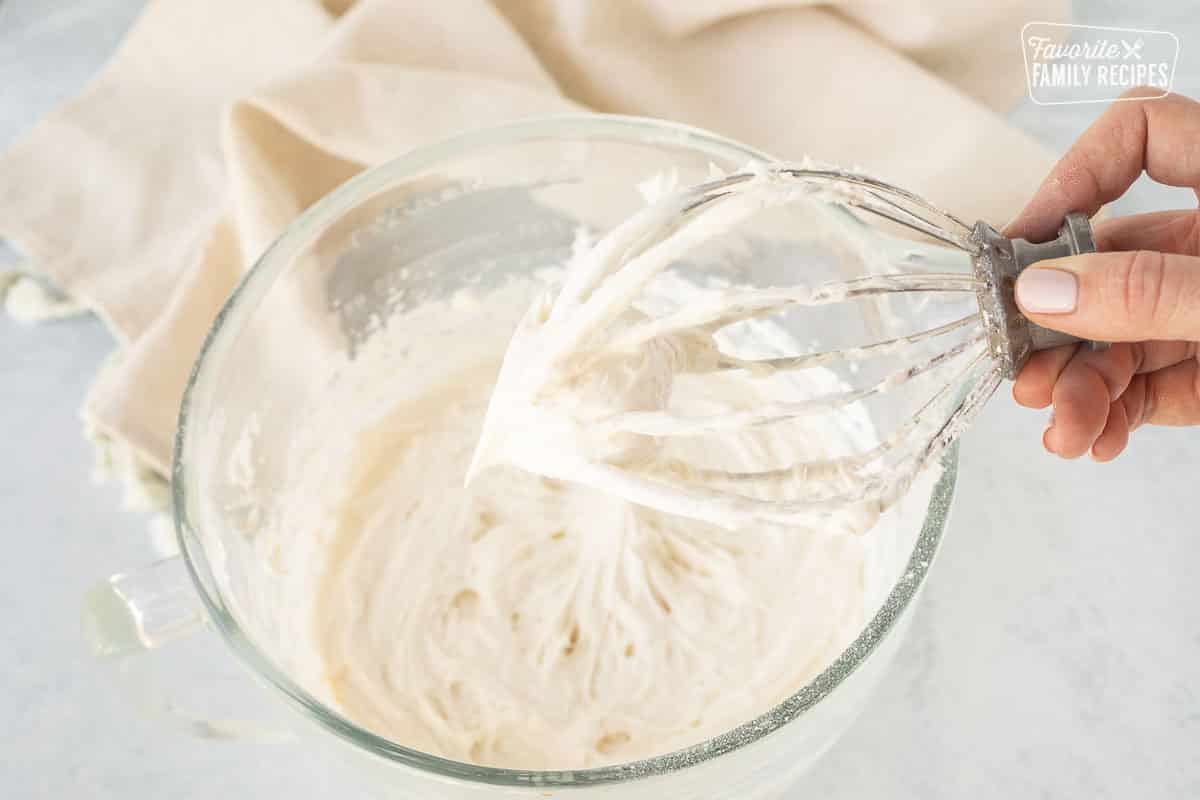 Hand holding up a whisk with cream cheese frosting.