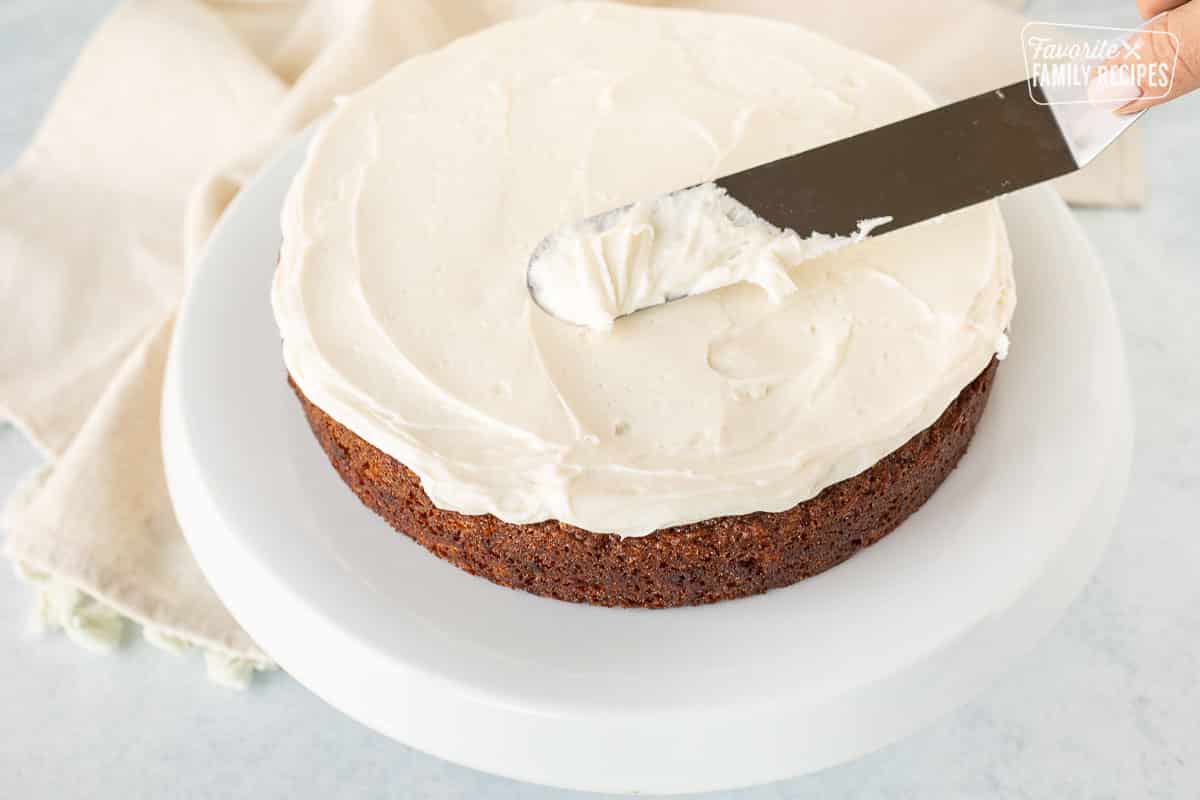 Spreading cream cheese frosting on a carrot cake with a spatula.