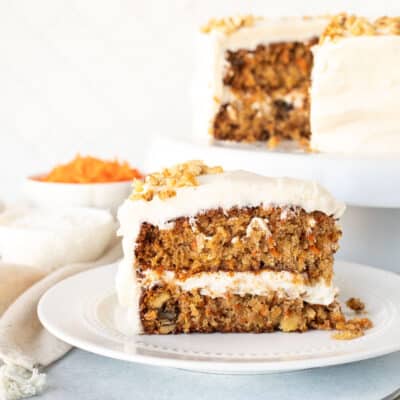 Slice of Classic Carrot Cake on a plate. Cake in the background on a stand.