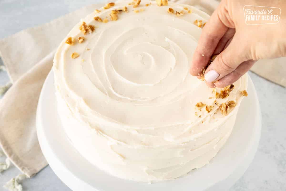 Sprinkling chopped walnuts on top of a frosted carrot cake.