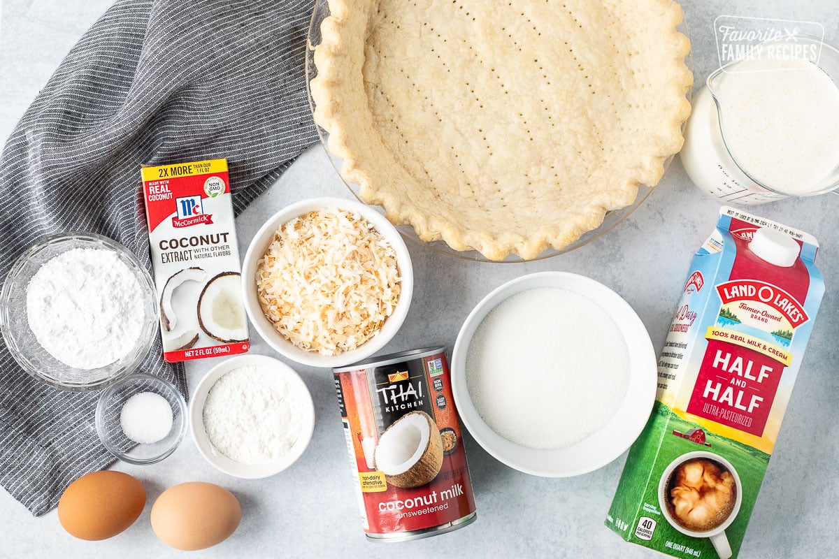 Ingredients to make Coconut Cream Pie including a pie crush, half and half, whipping cream, sugar, toasted coconut, coconut milk, corn starch, salt, eggs, coconut extract and flour.