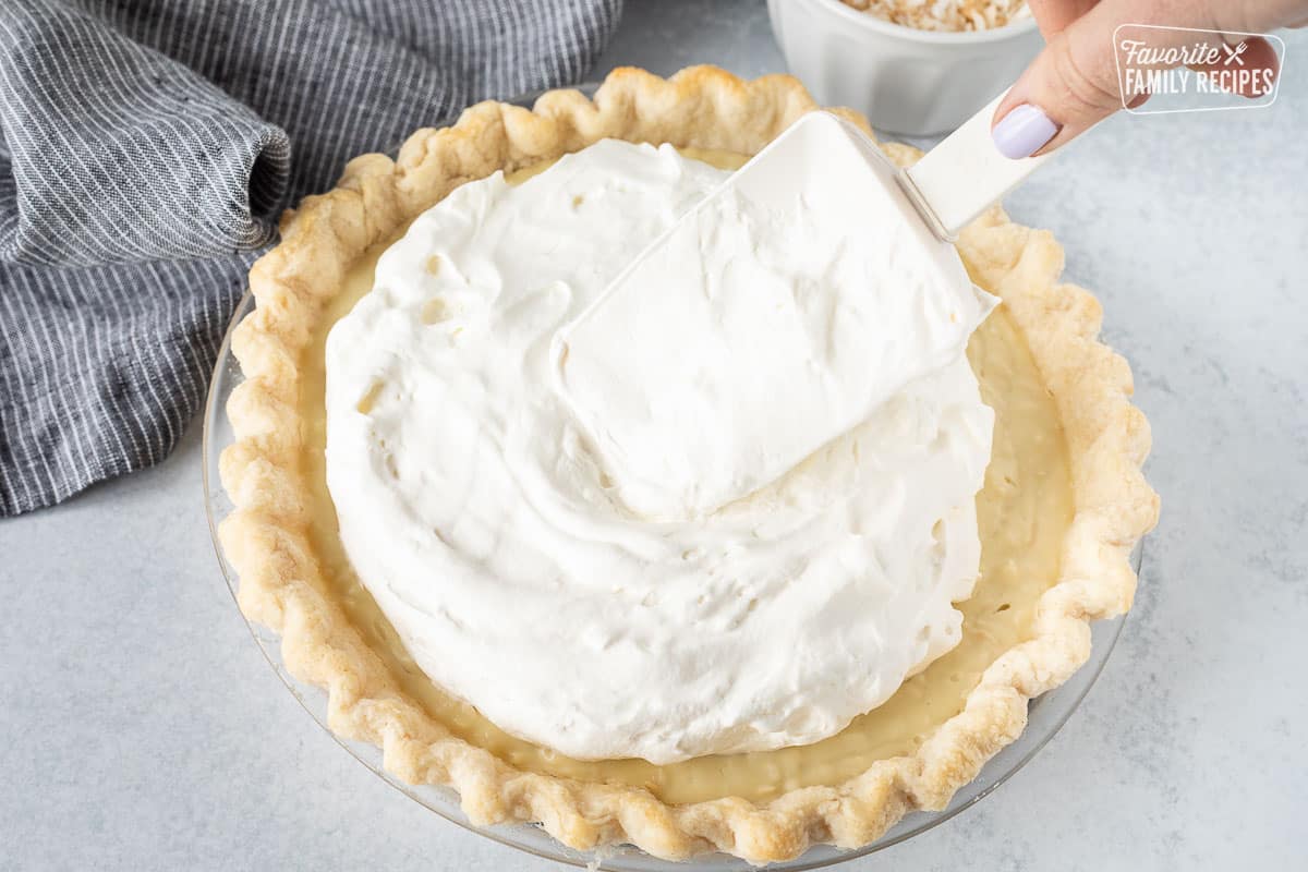 Spreading whipped topping on a Coconut Cream Pie with a spatula.
