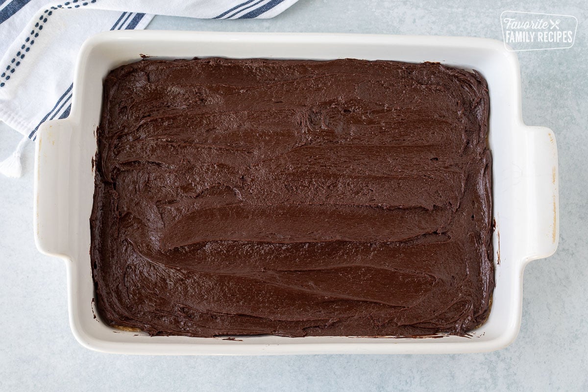 Spread chocolate fudge on top of cookie crust in a baking dish.