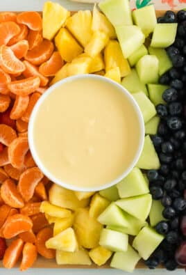 Cream cheese fruit dip on a platter with strawberries, orange slices, pineapple, honeydew, blueberries, and grapes