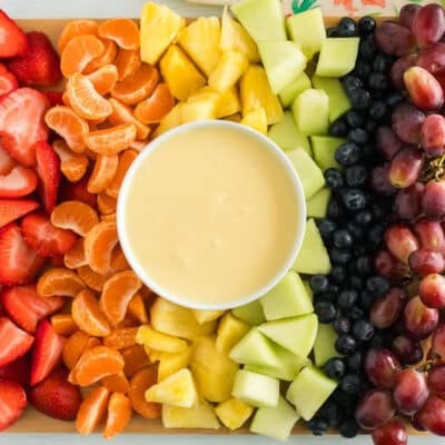 Cream cheese fruit dip on a platter with strawberries, orange slices, pineapple, honeydew, blueberries, and grapes