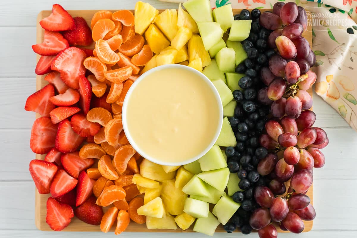 Cream cheese fruit dip on a platter with strawberries, orange slices, pineapple, honeydew, blueberries, and grapes.