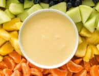 Cream cheese fruit dip on a platter with strawberries, orange slices, pineapple, honeydew, blueberries, and grapes