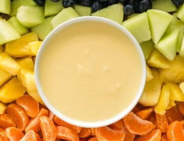 Cream cheese fruit dip on a platter with strawberries, orange slices, pineapple, honeydew, blueberries, and grapes