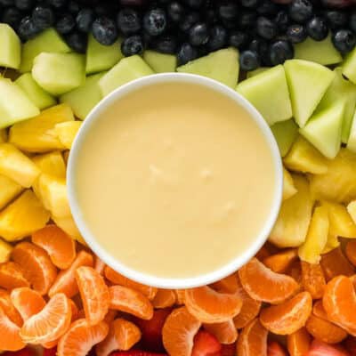 Cream cheese fruit dip on a platter with strawberries, orange slices, pineapple, honeydew, blueberries, and grapes