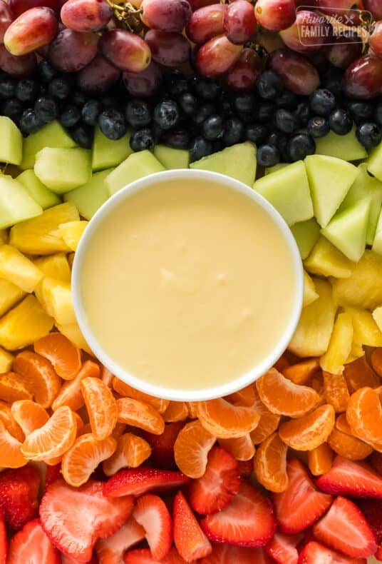 Cream cheese fruit dip on a platter with strawberries, orange slices, pineapple, honeydew, blueberries, and grapes