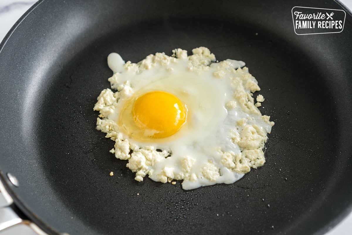 an egg cracked in a ring of feta cheese in a pan