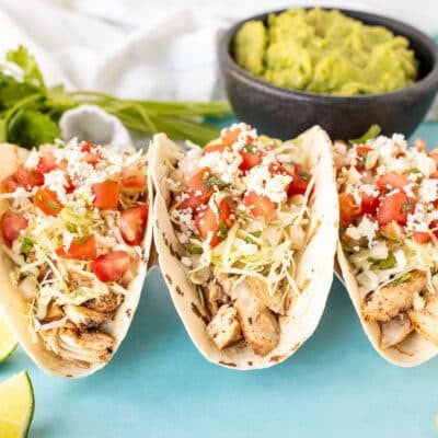 Front view of Three Grilled Mahi Mahi fish tacos with cabbage, pico and cheese. Guacamole, pico and chips on the side.