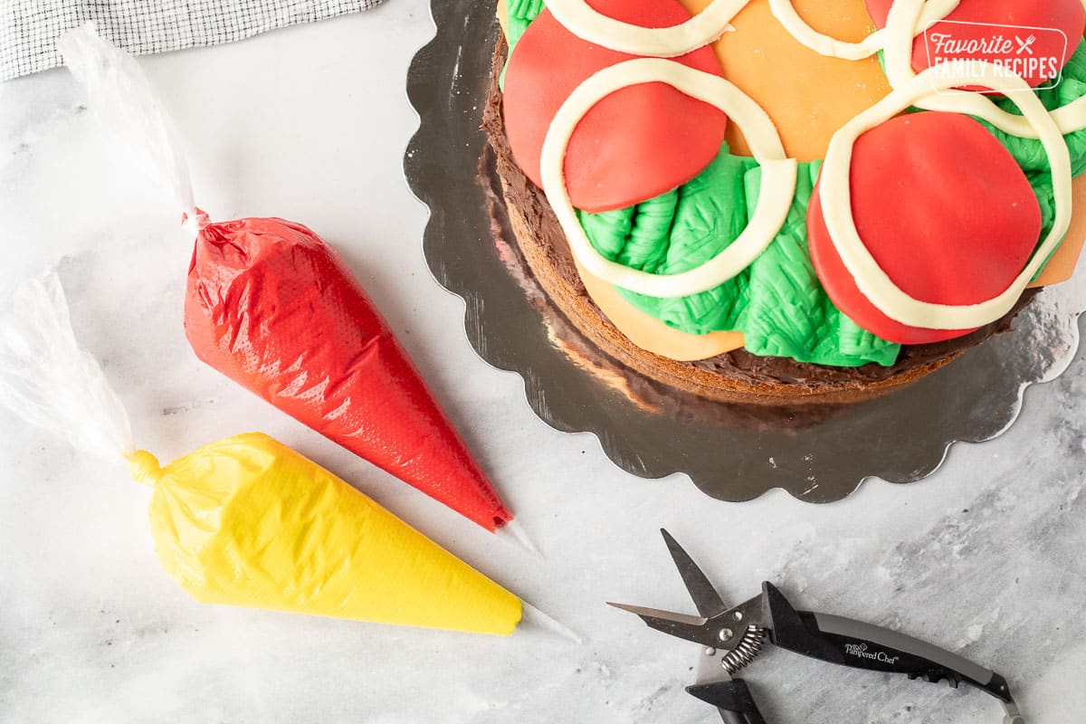 Yellow and red bags of frosting with scissors. Hamburger cake on the side.
