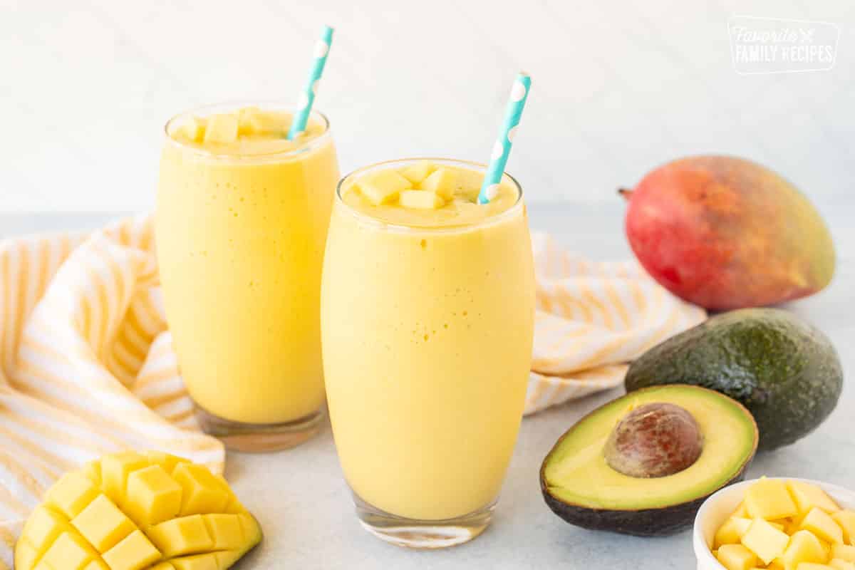 Two Mango Avocado Smoothies with Fresh Mano and Avocado on the sides.