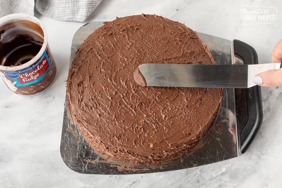 Spreading chocolate frosting on a chocolate cake with a spatula.