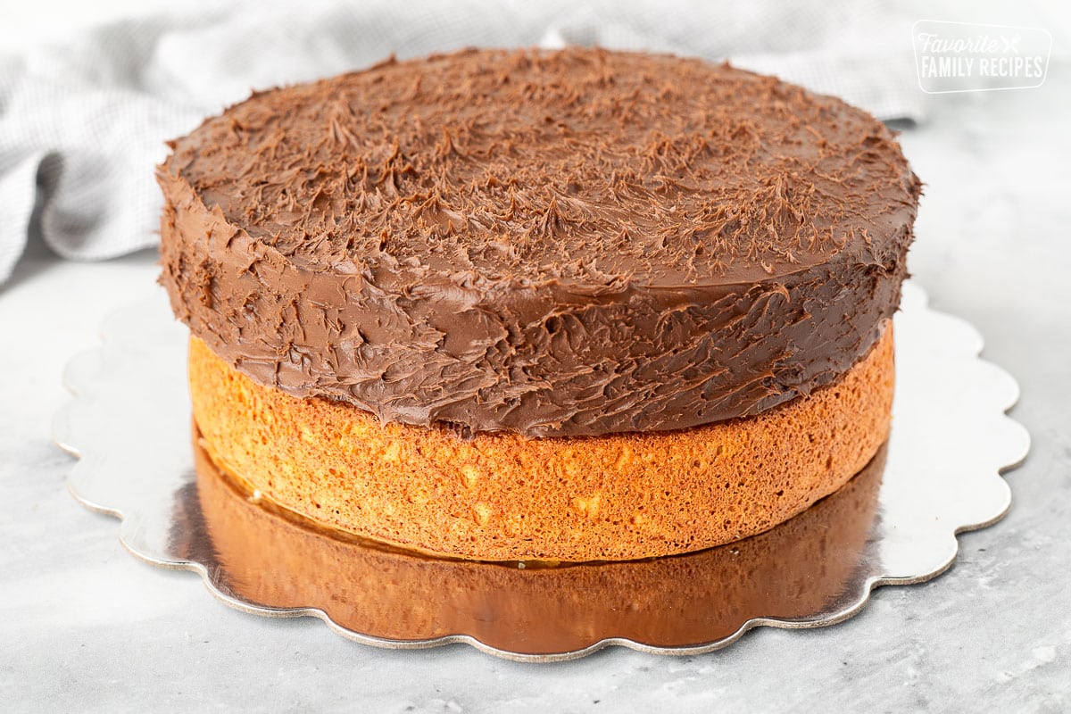 Chocolate frosted round cake on top of a yellow round cake.