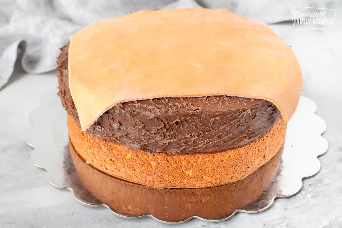 Piece of orange square fondant on top of chocolate frosted round cake.
