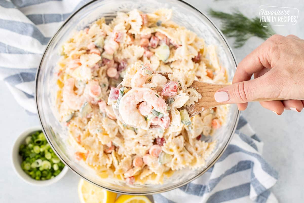 Hand holding a wooden spoon with a scoop of Shrimp Pasta Salad over the bowl of Shrimp Pasta Salad.