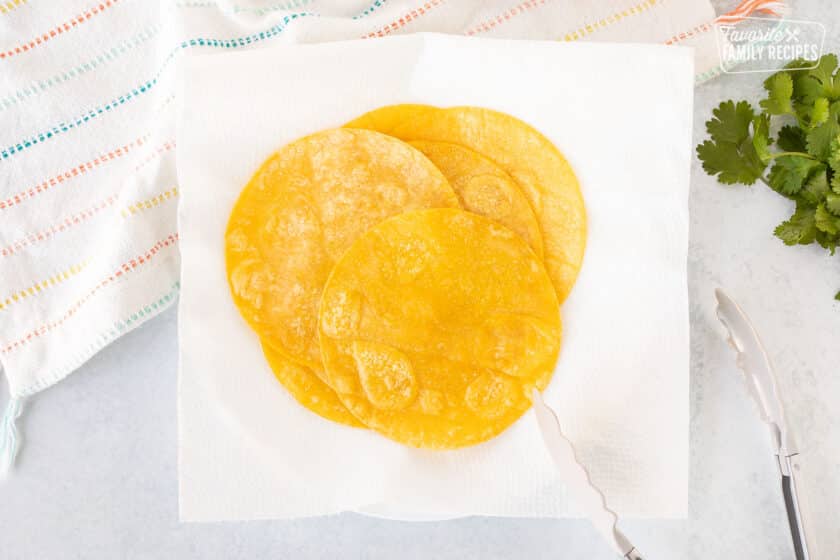 Fried corn tortillas on paper towels and tongs.