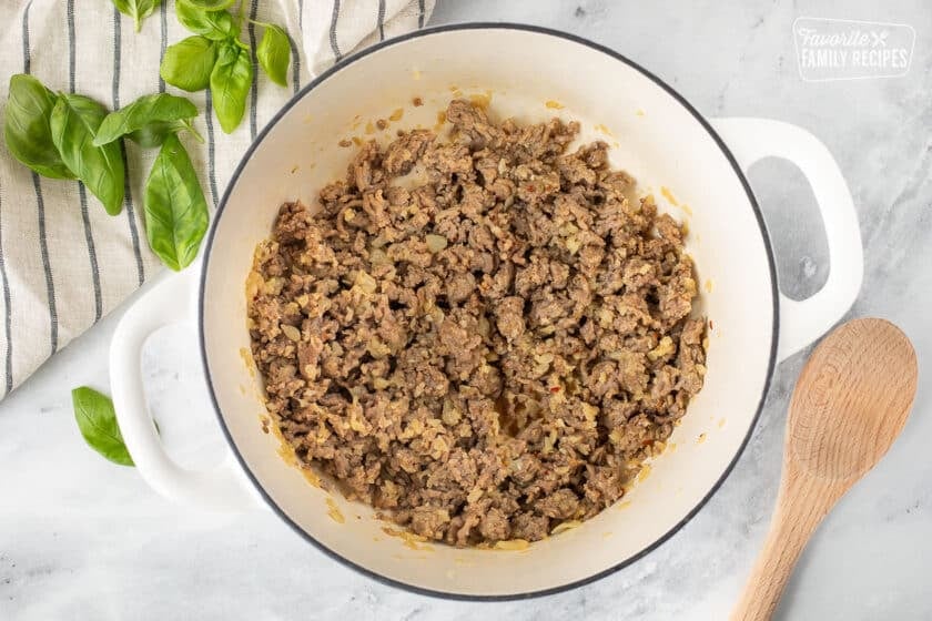 Ground mild Italian sausage browned in a pan. Wooden spoon on the side.