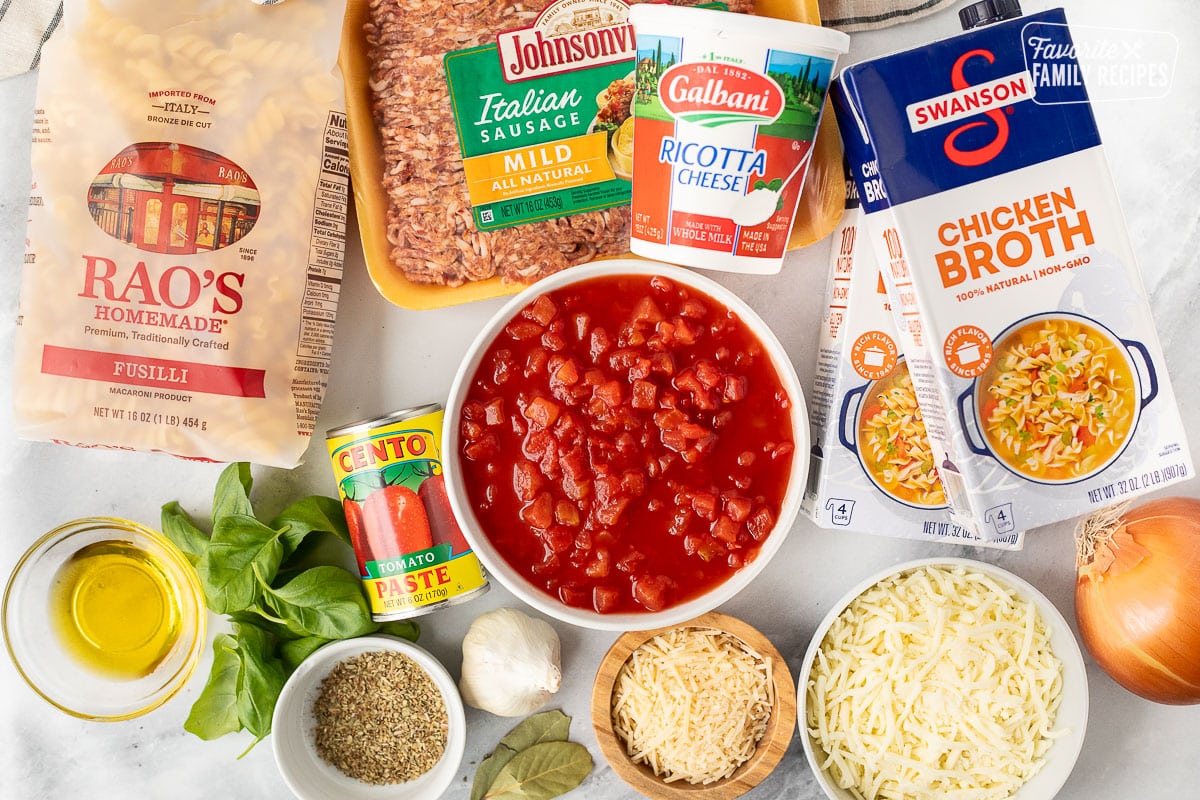 Ingredients to make Lasagna Soup with fusilli, Italian sausage, ricotta cheese, chicken broth, onion, mozzarella cheese, Parmesan cheese, bay leaves, garlic, diced tomatoes, tomato paste, oregano, red pepper flakes, fresh basil and olive oil.