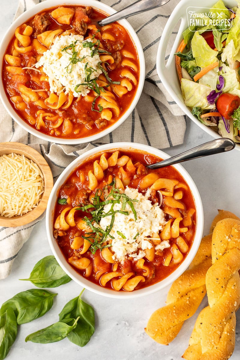 Two bowls of Lasagna Soup with bread sticks and salad.