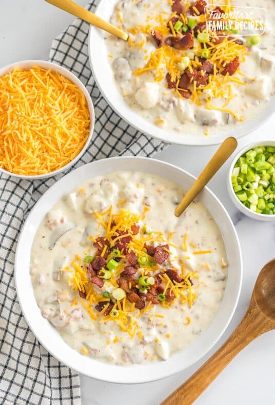 two bowls of loaded baked potato soup topped with bacon, cheese, and green onions